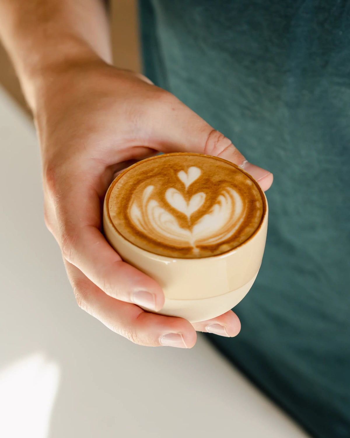 Handen houden een lichte kop cappuccino met latte art