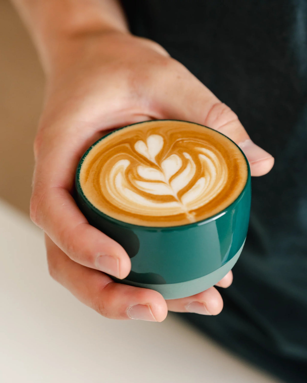 Handen houden een groen kopje cappuccino met latte art