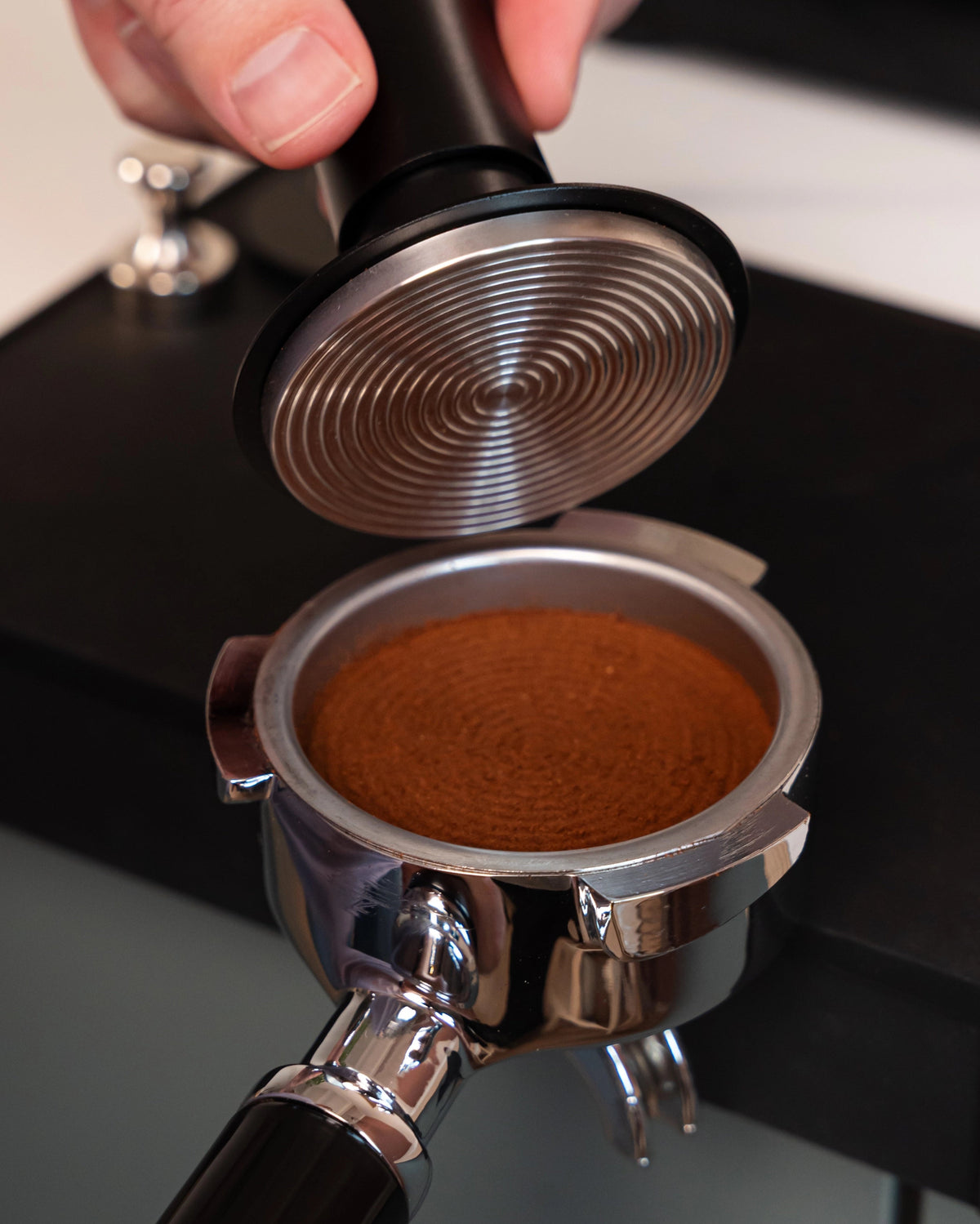Geribbeld tampvlak van de 58 mm klik-tamper boven aangedrukte koffie