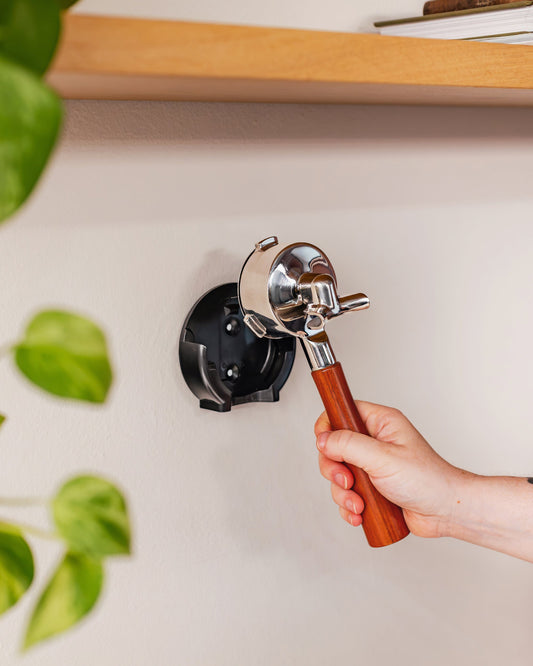 Een hand plaatst een portafilter in de 58 mm wandhouder