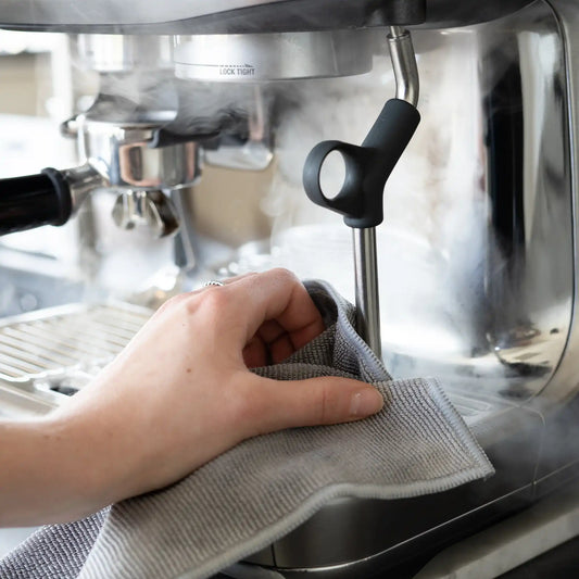 Hand van thuisbarista reinigt stoompijp van espressomachine met barista doekje na het melk opschuimen