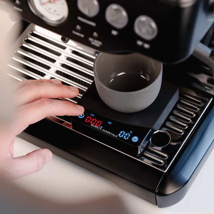 Thuisbarista zet espresso met koffieweegschaal onder espressomachine – ideale tool voor je eigen koffiecorner