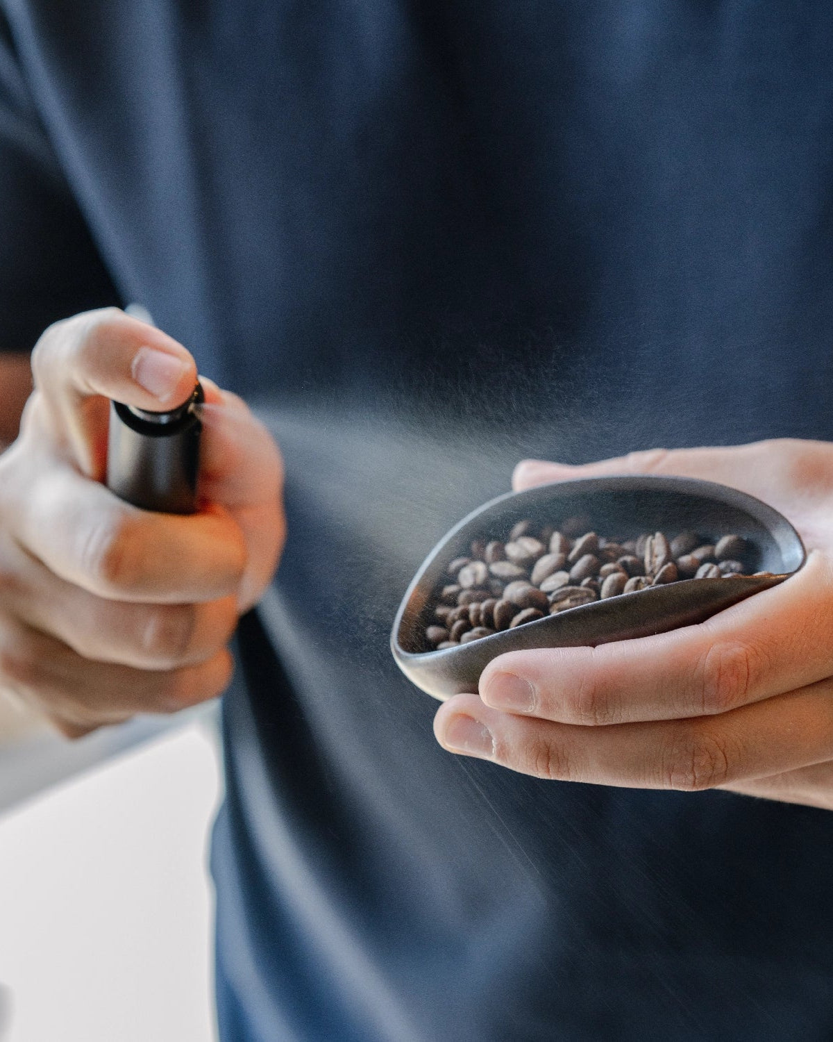 Een fijne nevel uit de RDT Spray boven koffiebonen in een doseerbakje