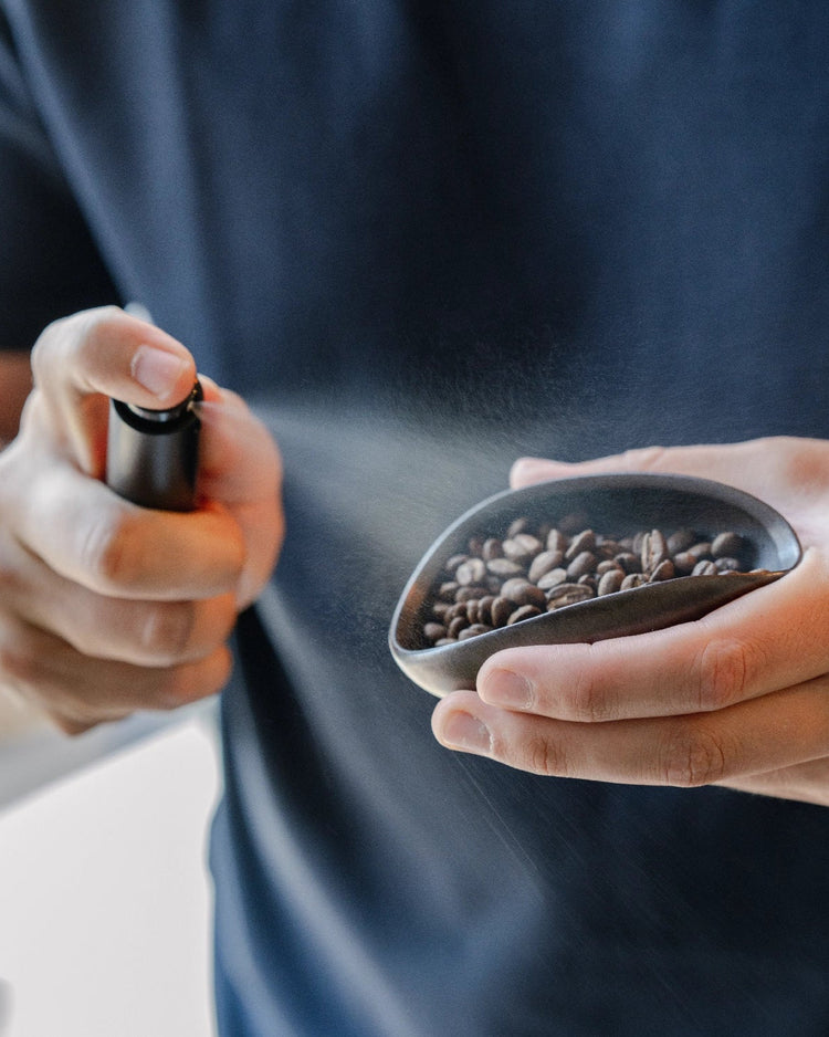 Een fijne nevel uit de RDT Spray boven koffiebonen in een doseerbakje