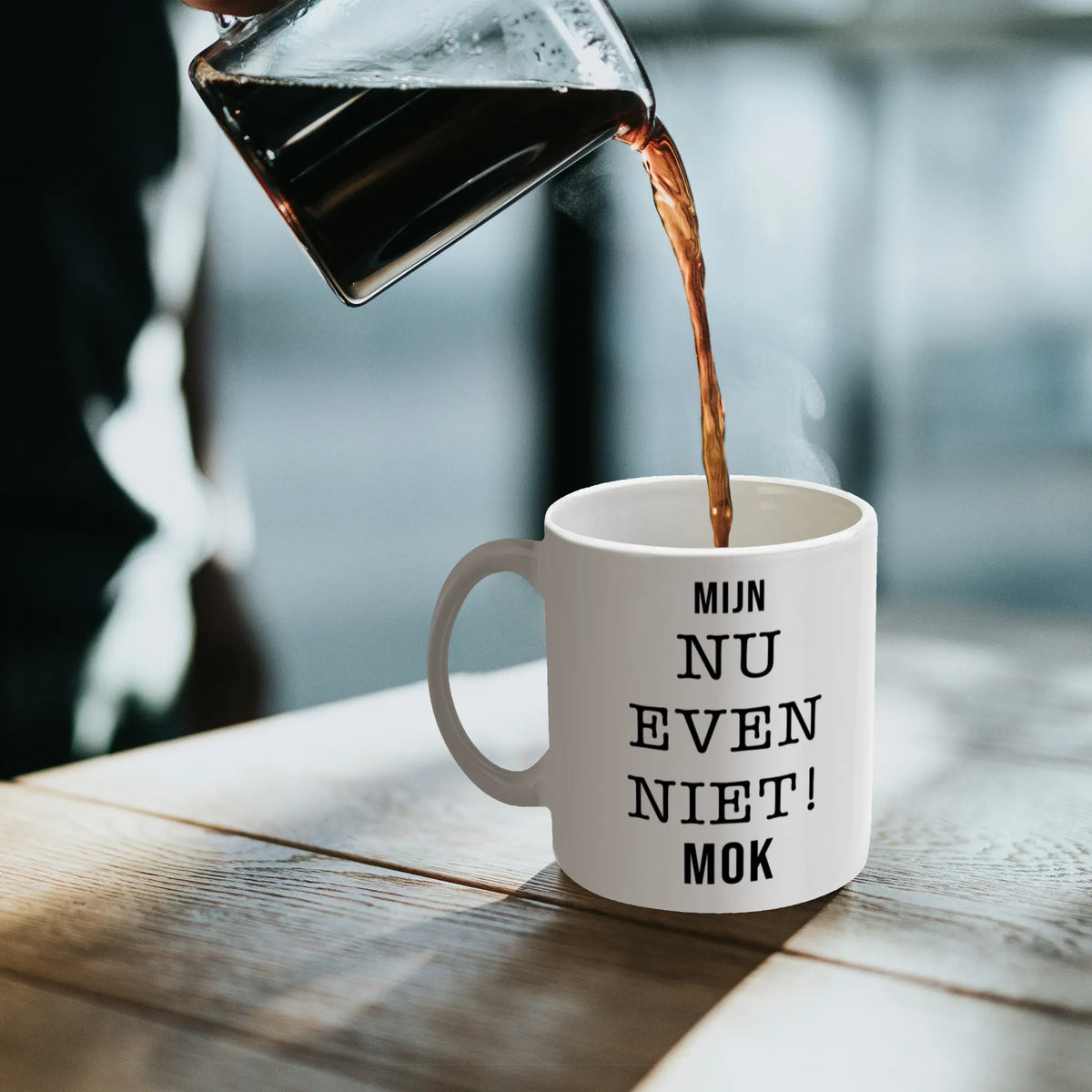 Witte keramische koffiemok met grappige tekst op een bureau, geschikt als origineel koffiecadeau voor een collega op werk.