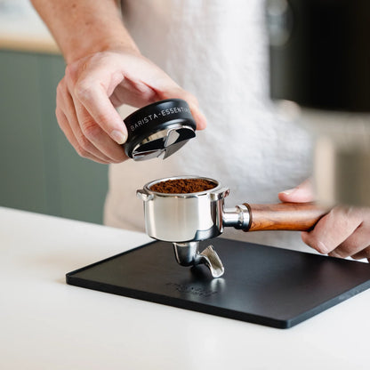 Zwarte koffieverdeler boven een filterdrager op een tampingmat