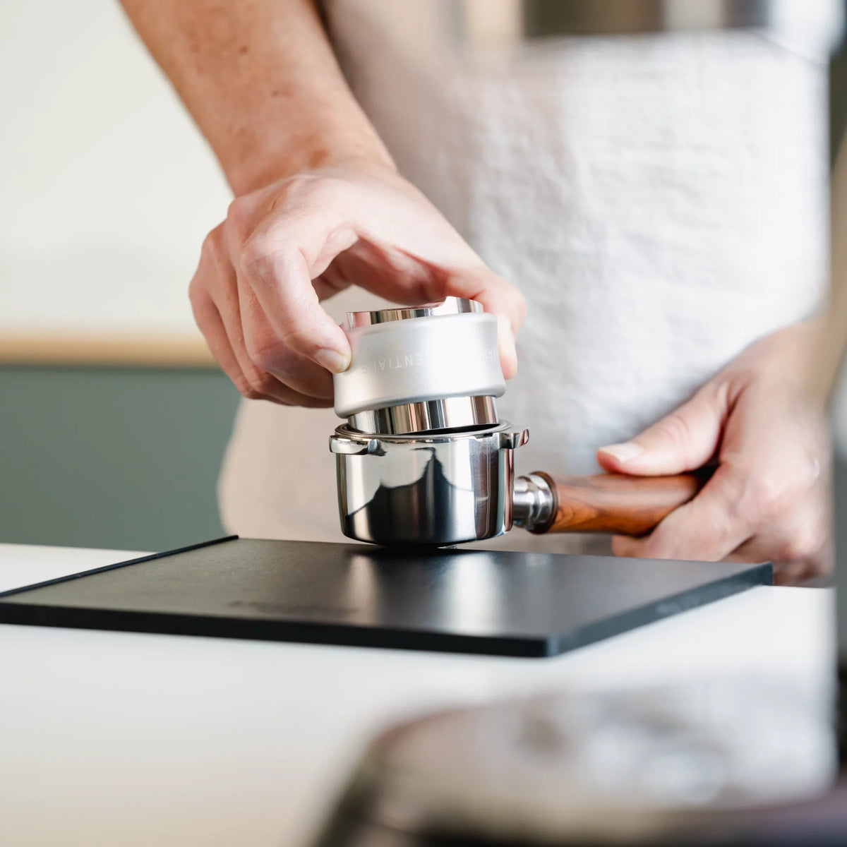Zilveren combinatietool in een portafilter boven een tampingmat