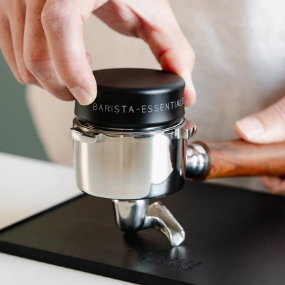 Hand plaatst een zwarte koffieverdeler in een portafilter