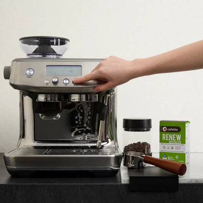 Een hand bedient een espressomachine met Cafetto Renew ernaast