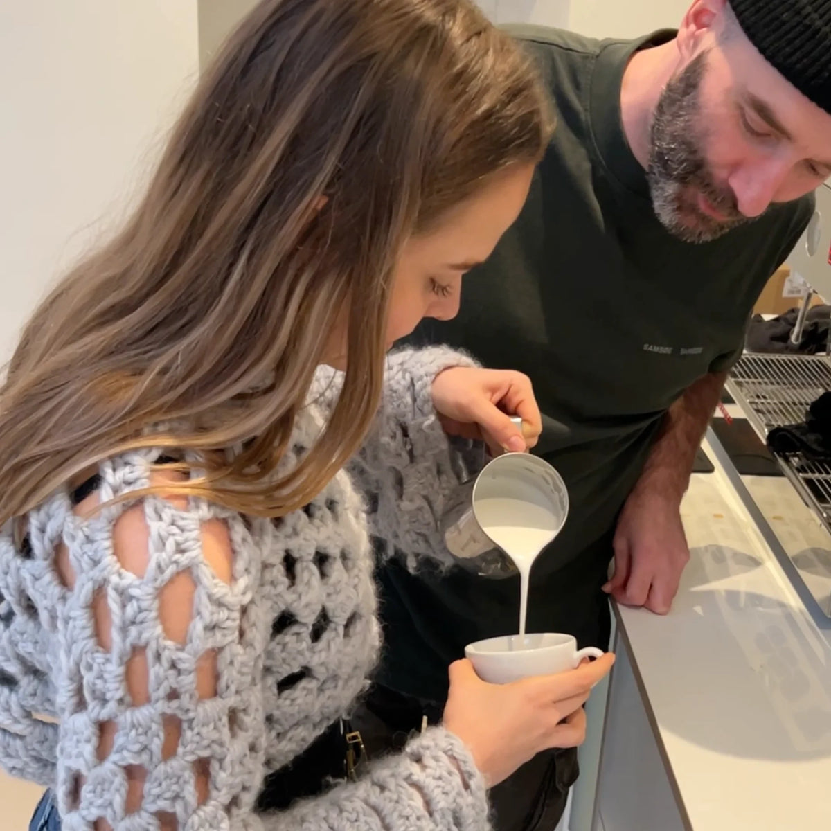 Coach kijkt mee terwijl een deelneemster melk uitschenkt voor haar eerste latte art creatie.