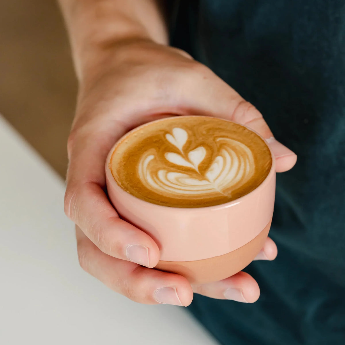 Handen houden een roze kop cappuccino met latte art