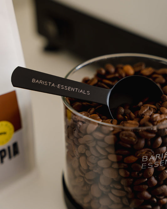 Koffiebonen scheppen uit een glazen voorraadbus