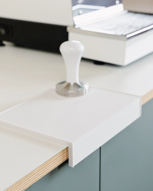 De grote witte tampermat met hoek op de rand van het werkblad met een tamper