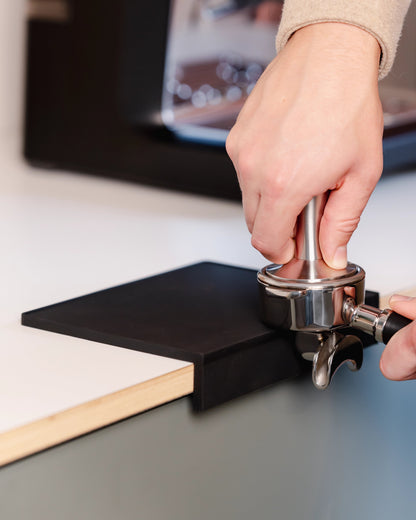 Koffie aandrukken met een portafilter op de grote zwarte tampermat met hoek