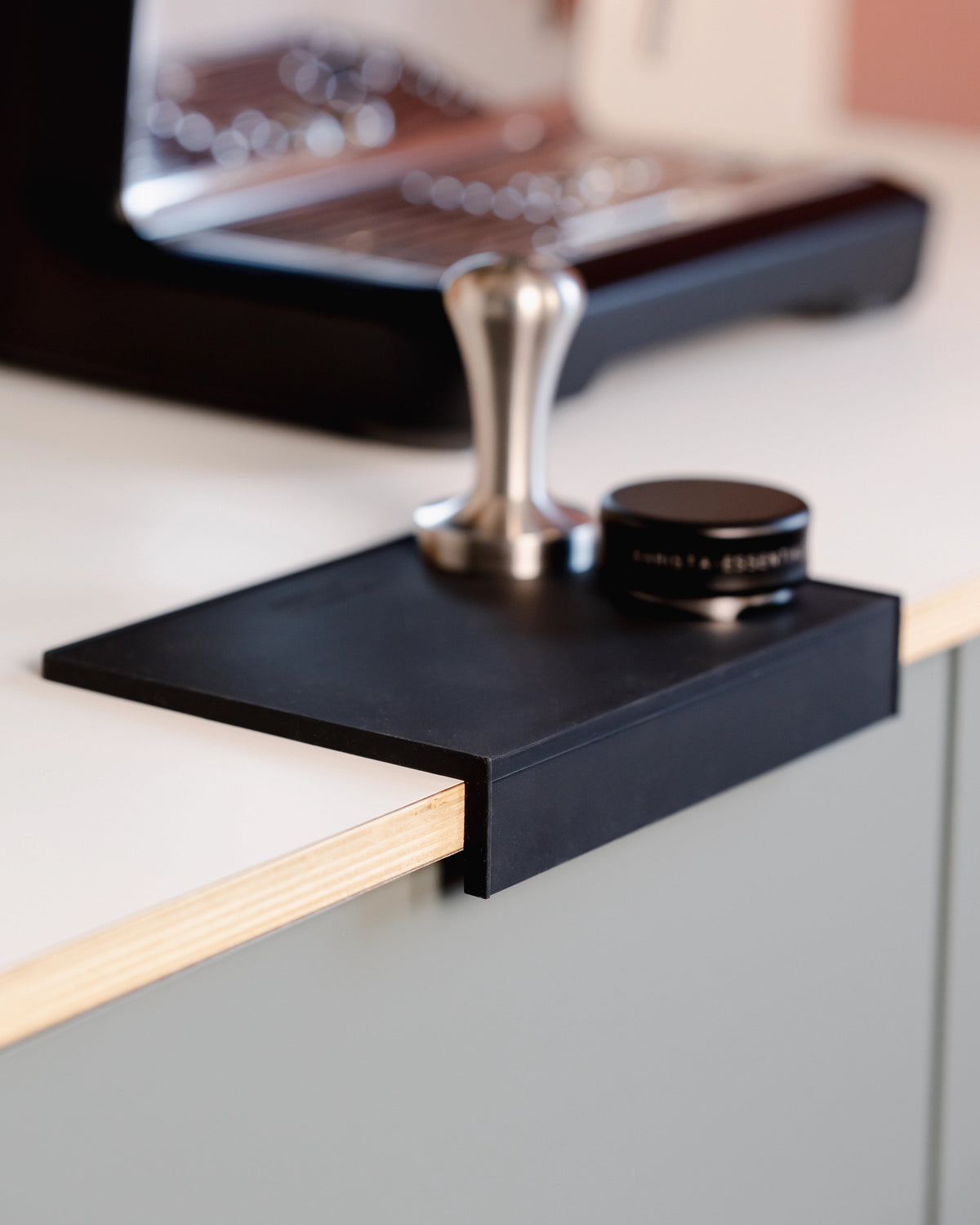 Een tamper op de grote zwarte tampermat met hoek naast de espressomachine