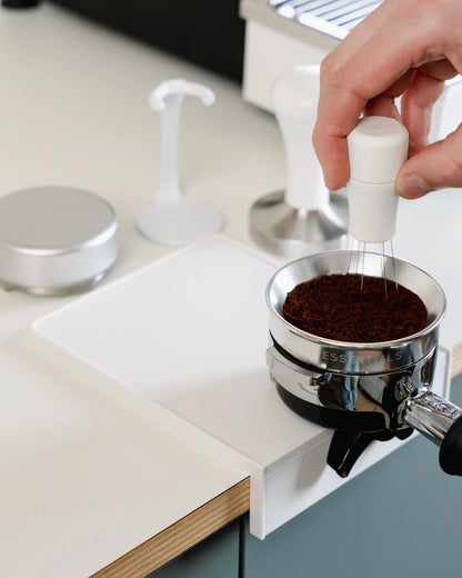Koffie aandrukken op de kleine witte tampermat met hoek