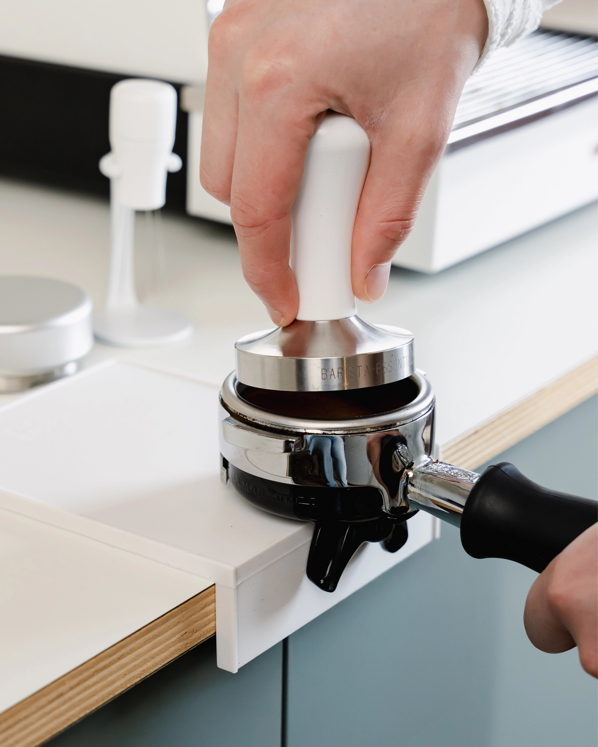 Een portafilter en tamper boven de kleine witte tampermat met hoek