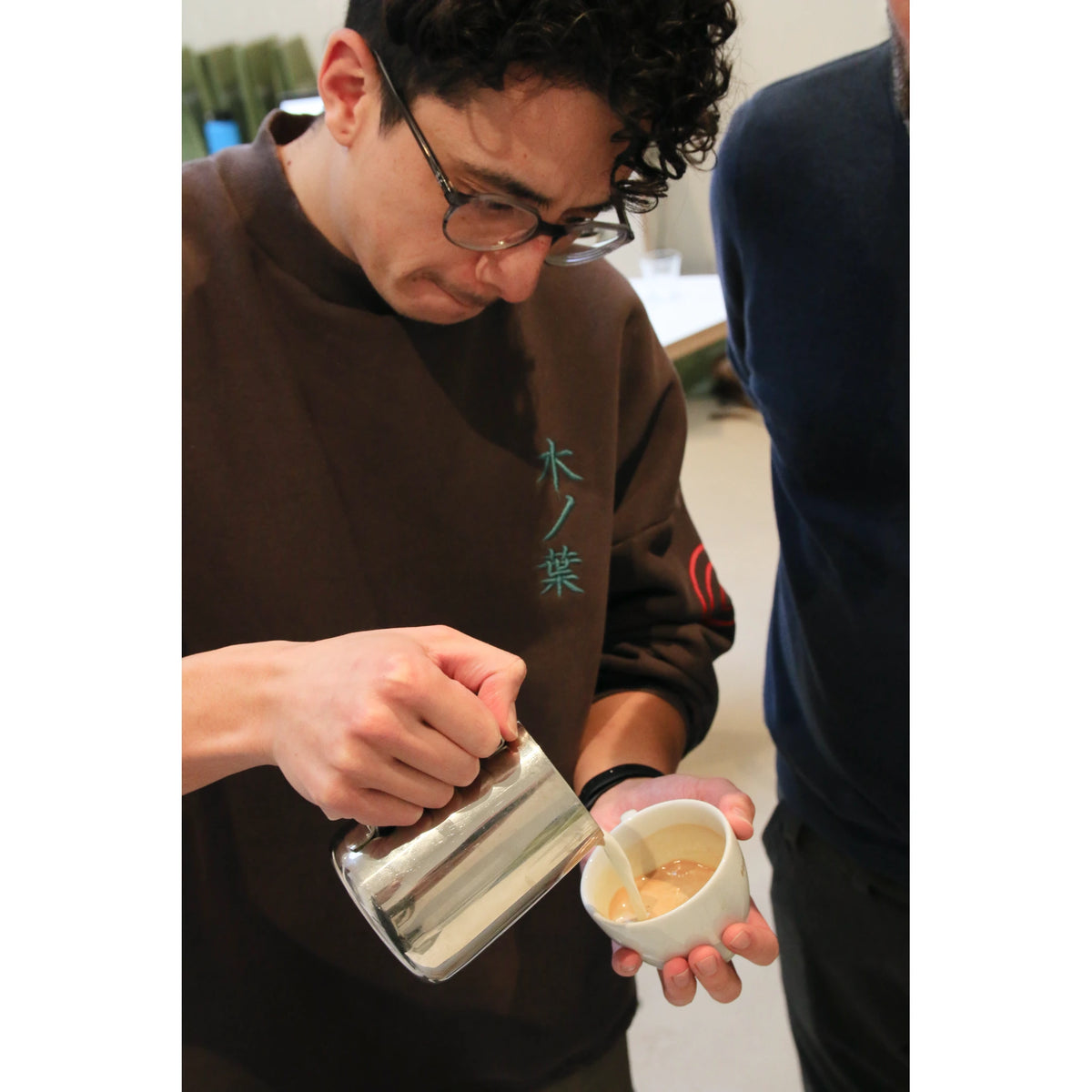 Close-up van een deelnemer die melk uitschenkt in een kopje om een latte art patroon te maken.