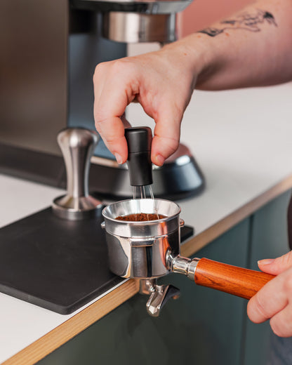 Zilveren doseerring van 51 mm op een filterdrager tijdens het verdelen van gemalen koffie