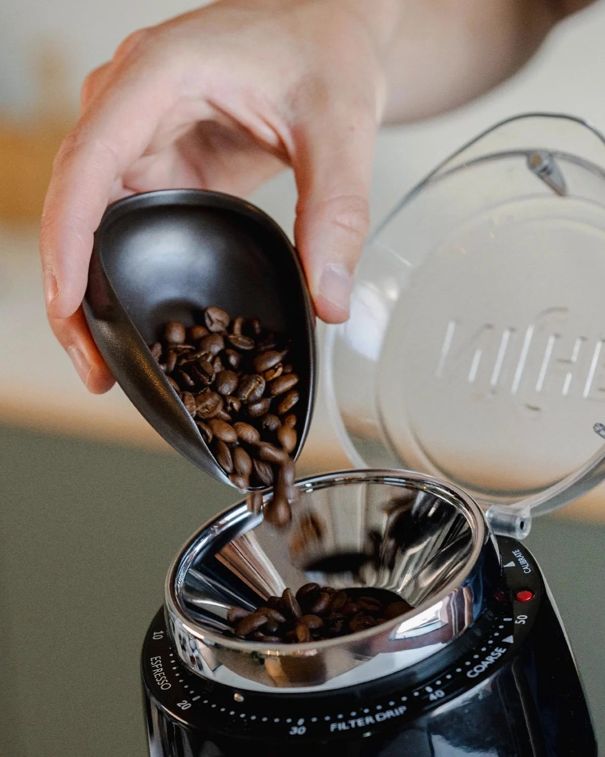 Koffiebonen worden via de tuit van een zwarte doseerschaal in een molen gegoten
