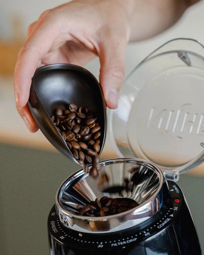 Koffiebonen worden via de tuit van een zwarte doseerschaal in een molen gegoten