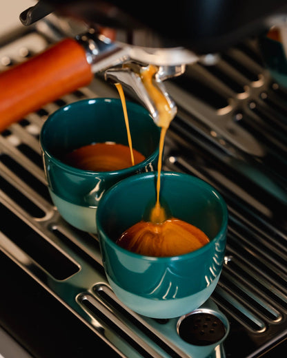 Espresso stroomt in twee groene kopjes onder een portafilter