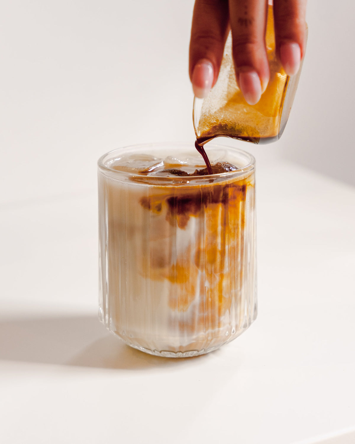 Espresso wordt in een geribbeld glas met melk en ijs geschonken