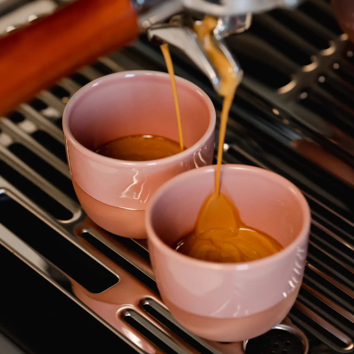 Espresso stroomt in roze kopjes onder de machine-uitloop