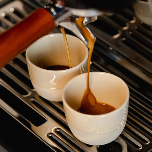 Espresso stroomt in zandgele kopjes onder de machine-uitloop