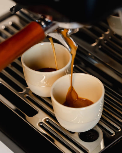 Espresso stroomt in twee lichte kopjes onder een portafilter