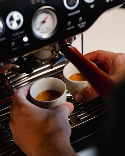 Hand houdt een gestippeld espressokopje onder een espressomachine