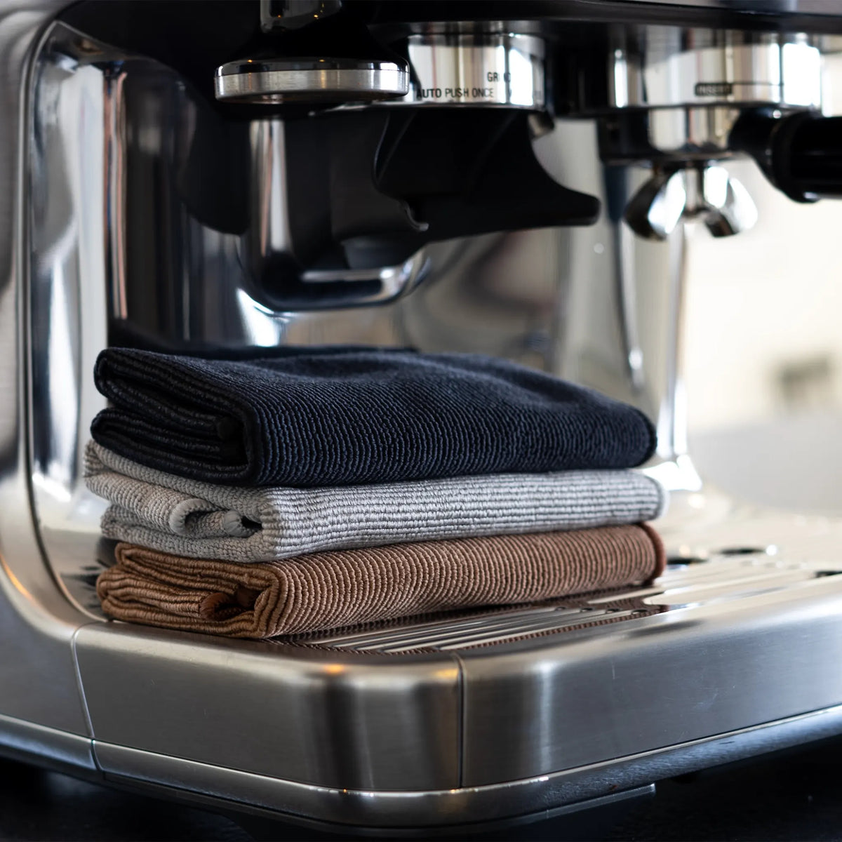 Gevouwen zwarte grijze en bruine doeken op de lekbak van een espressomachine