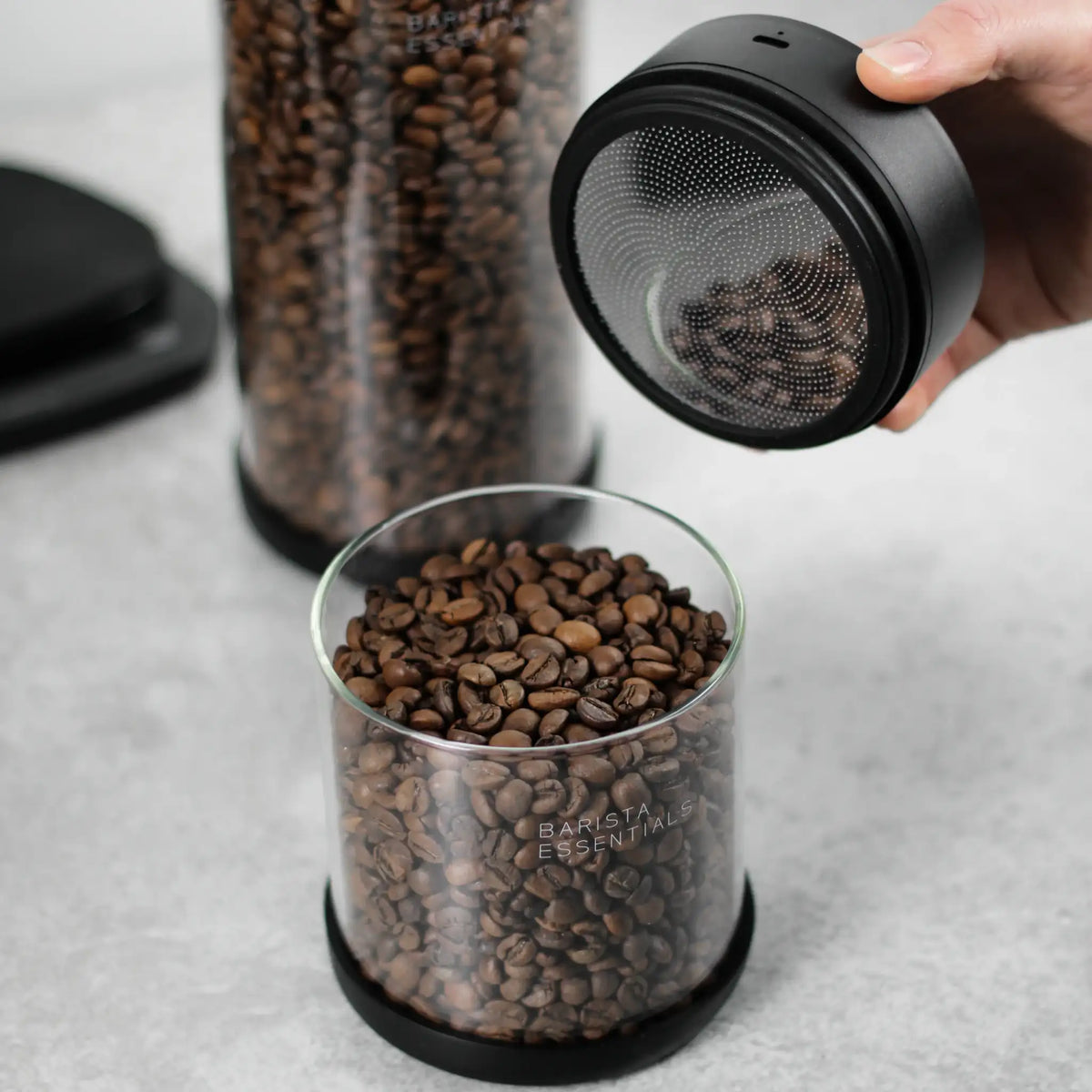 Hand tilt de zwarte deksel van een glazen koffiebus met bonen