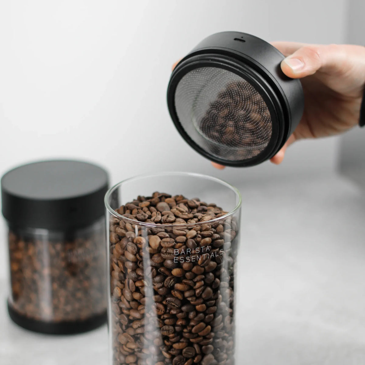 Hand tilt de Pro-deksel van een glazen koffiebus met koffiebonen