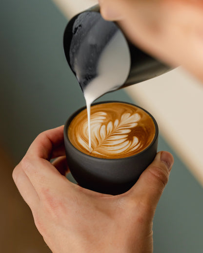 Melk wordt in een grijs cappuccinokopje geschonken