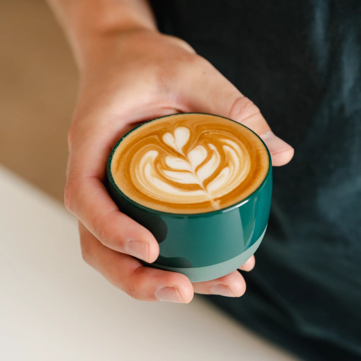 Hand houdt een groen kopje met latte art