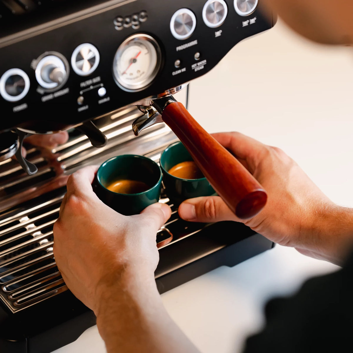 Hand houdt een groen kopje onder de uitloop van een espressomachine