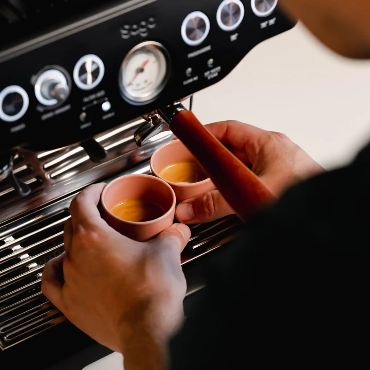 Hand houdt een roze kopje onder de espressomachine