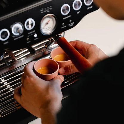 Hand houdt een roze kopje onder de espressomachine