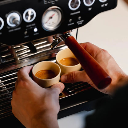 Hand houdt een zandgeel kopje onder de espressomachine