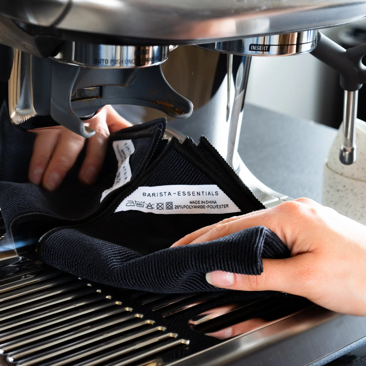 Hand houdt een zwarte doek bij de espressomachine