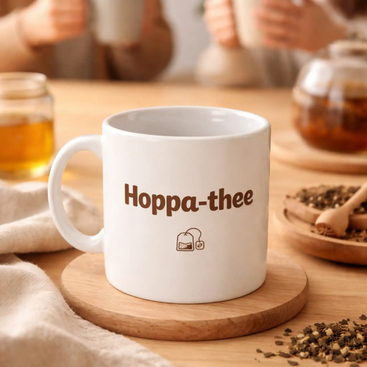 Sfeerbeeld van de Hoppa-thee mok op tafel, met mensen op de achtergrond die samen thee drinken in een warme en ontspannen setting.