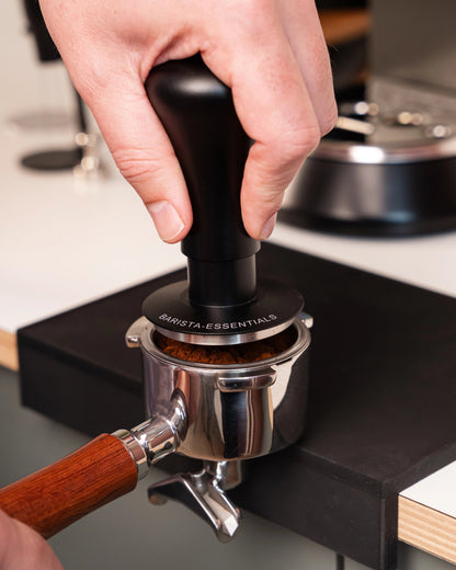 Hand drukt een zwarte 51 mm klik-tamper in een filterdrager