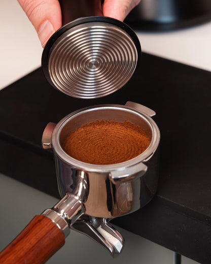 Geribbeld tampvlak van de 51 mm klik-tamper boven aangedrukte koffie