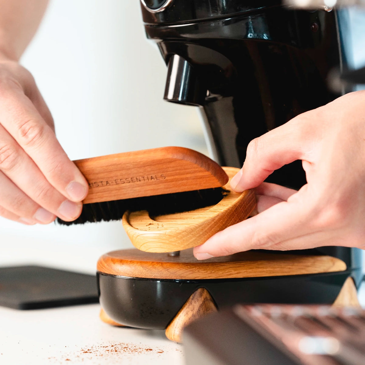 Hand veegt met een brede koffieborstel onder de espressomachine