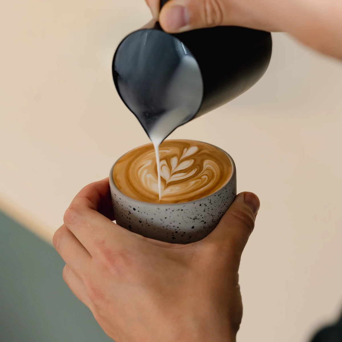 Melk wordt geschonken in espresso voor het oefenen van latte art – bovenaanzicht van barista in actie.