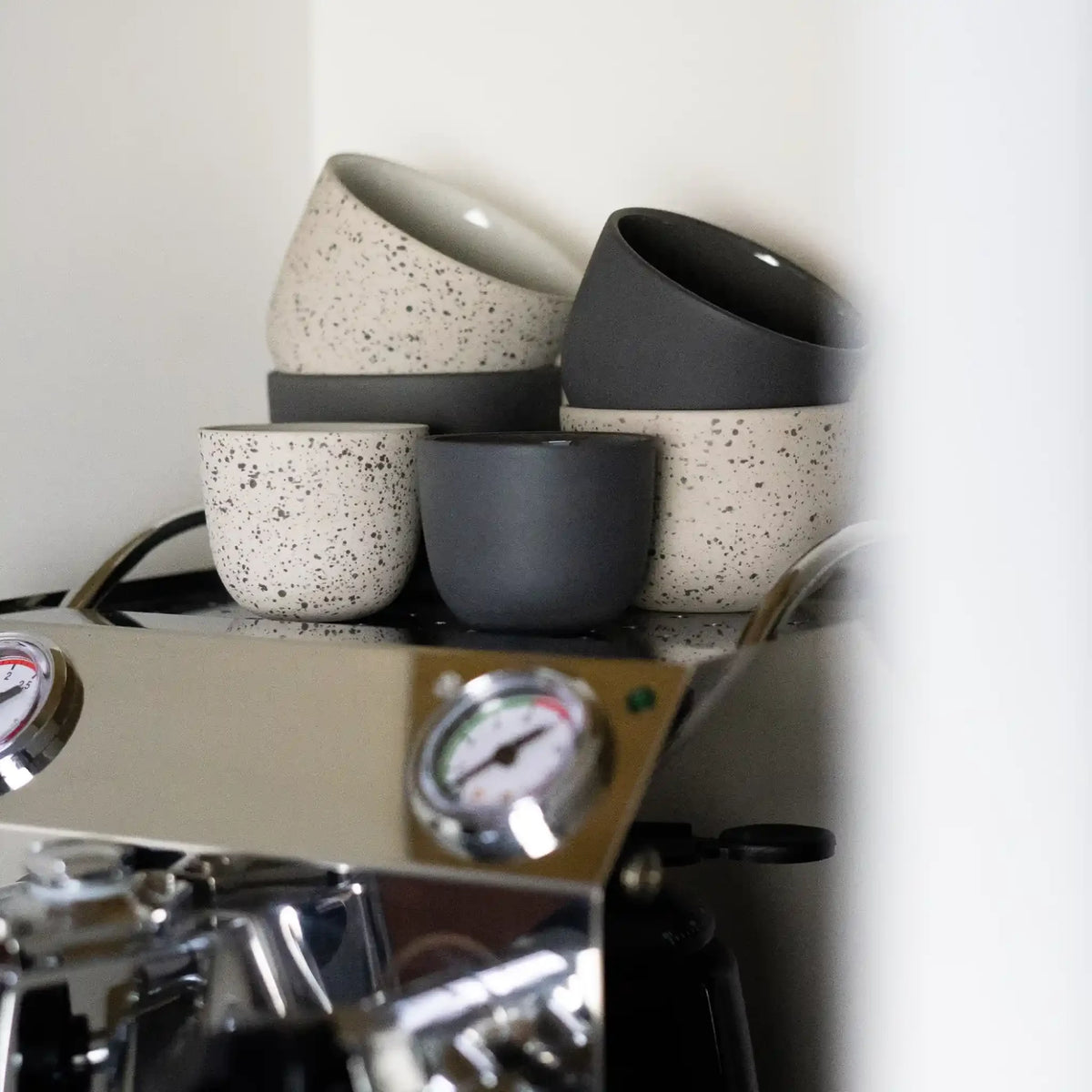 Latte kopjes in verschillende kleuren op aanrecht naast Sage Barista Express espressomachine.