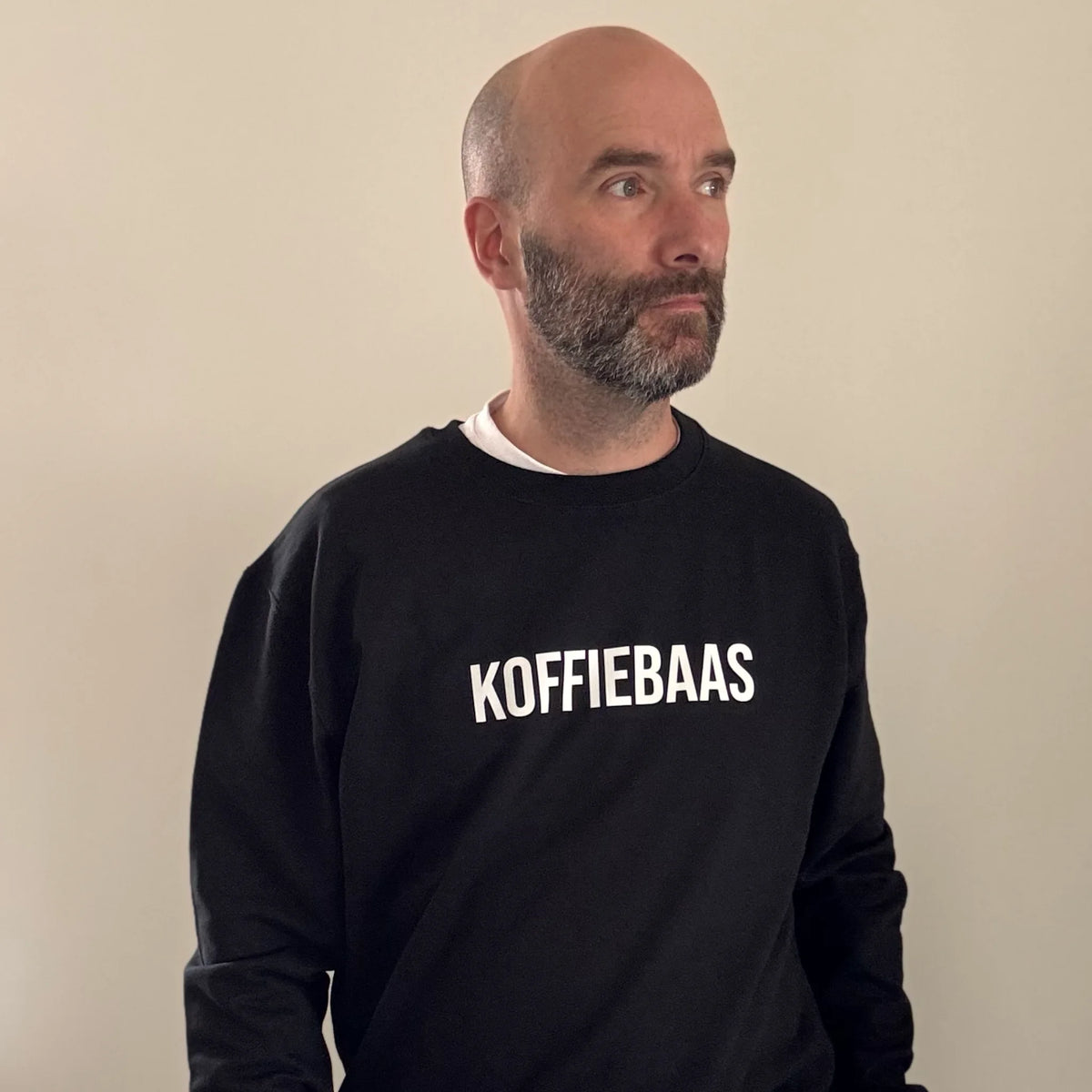 Volledige look van man in zwarte barista sweater met “KOFFIEBAAS” print