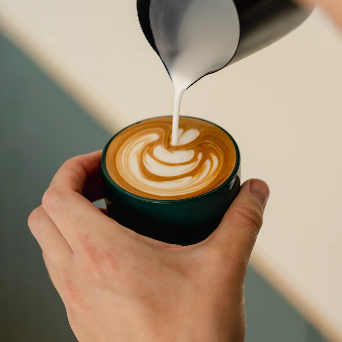 Melk wordt in een groen kopje geschonken voor latte art