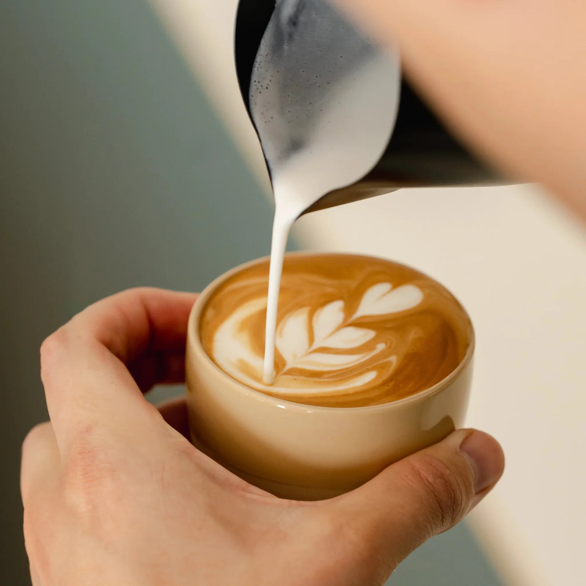 Melk wordt in een zandgeel kopje geschonken voor latte art